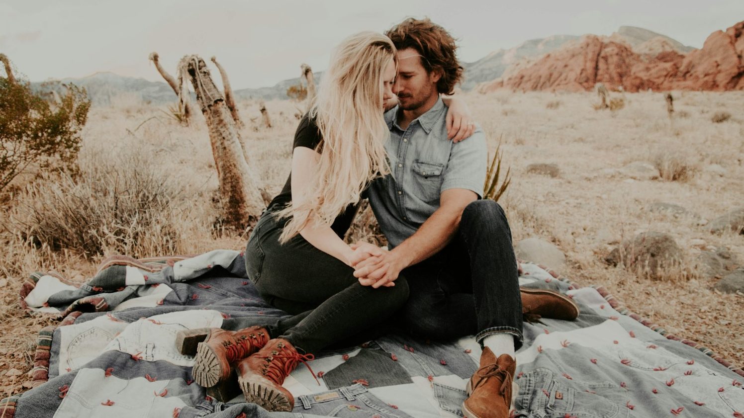 man and woman sitting on blanket while holding each other hands