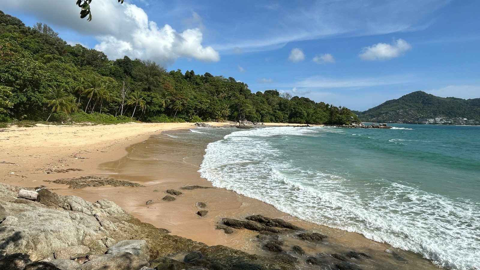 a sandy beach next to a lush green forest covered hillside