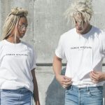 man and woman in white-and-gray force majeure-printed crew-neck t-shirts standing near gray concrete wall