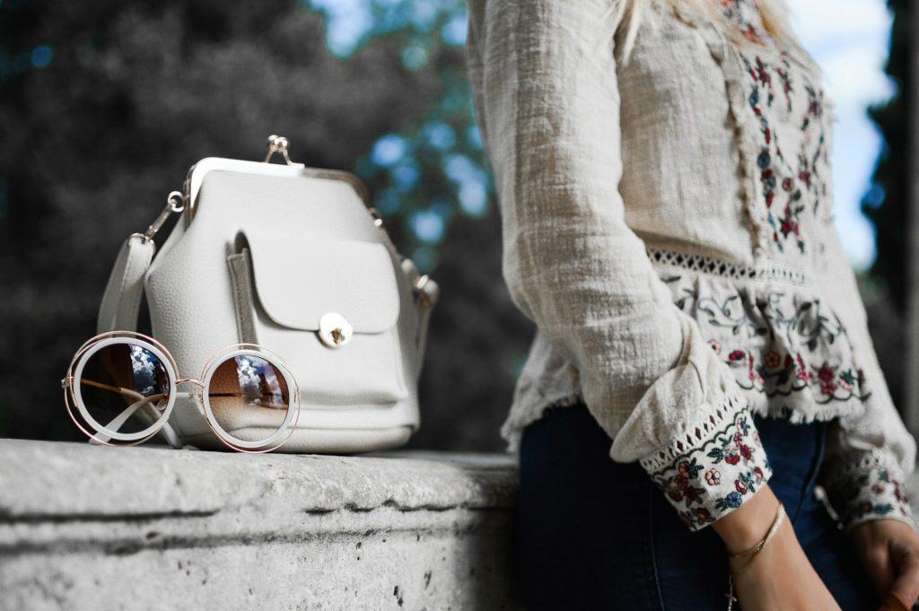 woman wearing beige and red floral top leaning on gray concrete slab with white leather bag ontop, 10 Most Stunning Fashion Trends for 2024