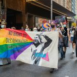 a group of people walking down a street holding a rainbow flag