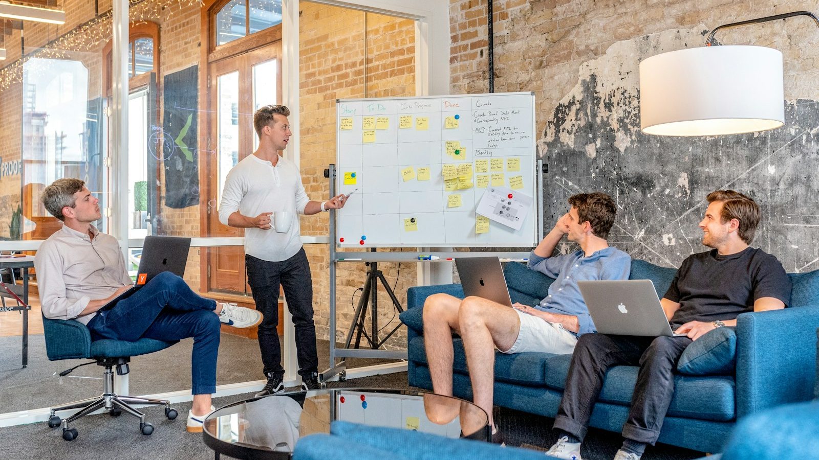 three men sitting while using laptops and watching man beside whiteboard