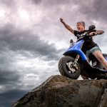 man in black jacket and blue denim jeans riding blue and white motorcycle