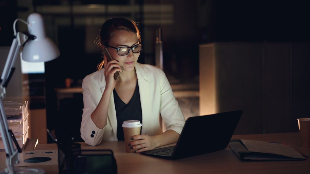 Woman talking on phone at desk with laptop and coffee. Monetary Efficiency Valuing Time Over Money