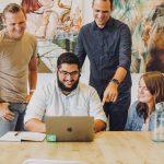 four coworkers smiling around laptop at table