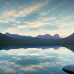 A photograph of a serene landscape featuring a calm lake surrounded by mountains at sunset