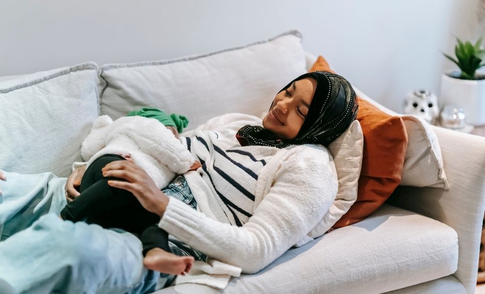 Woman in headscarf lying on sofa breastfeeding baby