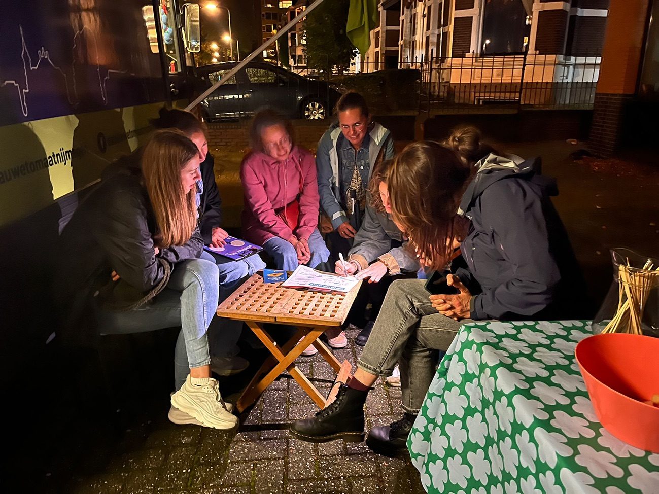Collega's zitten 's avonds buiten met elkaar gebogen over een spreekwoordenopdracht op een klein tafeltje