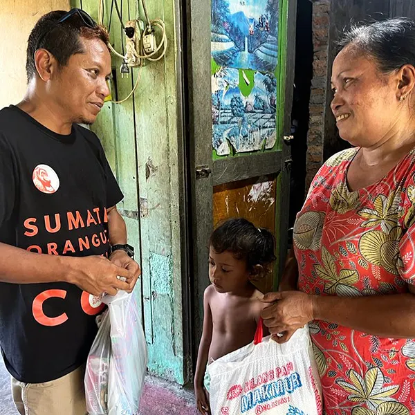 Indonesian guide from Sumatra Orangutan Trekking donating rice to a woman and books to her child, after an ethical Jungle Trekking tour.