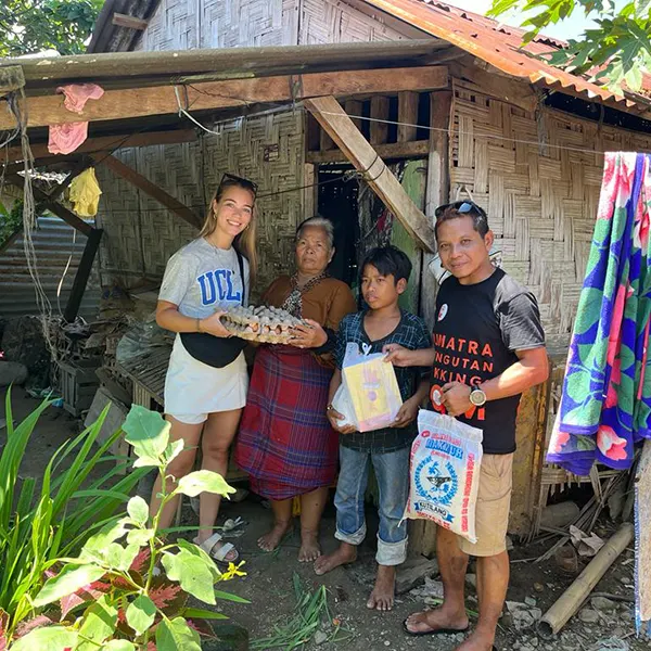 Woman tourist from Sumatra Orangutan Trekking donating rice, eggs and schoolbooks to an indonesian woman and her child