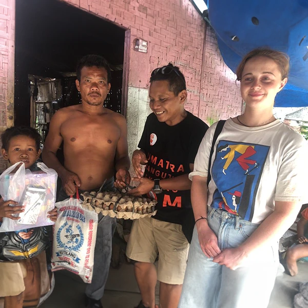 Tourist woman from Sumatra Orangutan Trekking donating rice, eggs and books to a family in need after an ethical jungle trekking.