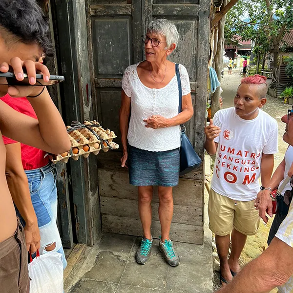 Tourist from Sumatra Orangutan Trekking donating egg and rice to an indonesian woman