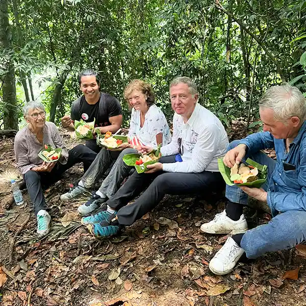 group of trekkers enjoying a meal on leaf plates during a rest on a sumatran jungle trek, with lush greenery surrounding them