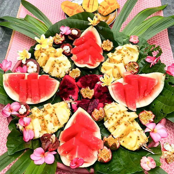 colorful array of fresh tropical fruits artistically arranged on green leaves, adorned with bright flowers, offering an inviting selection of watermelon, pineapple, mango, and dragon fruit