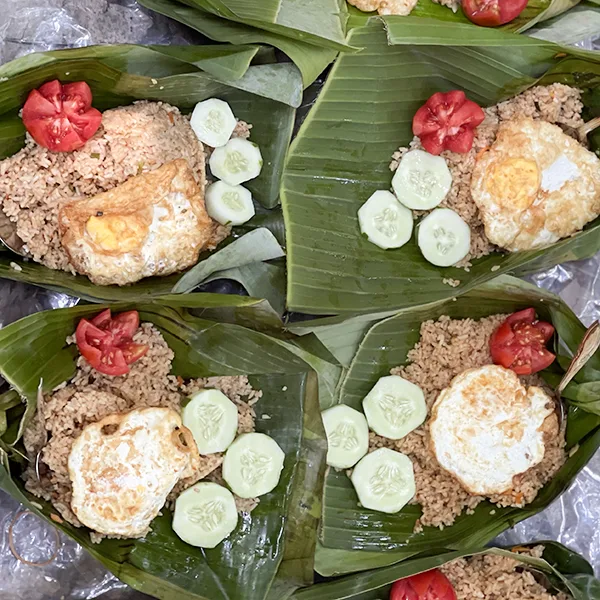 traditional indonesian meal served on banana leaves featuring brown rice, fried egg, fresh cucumber slices, and a tomato garnish