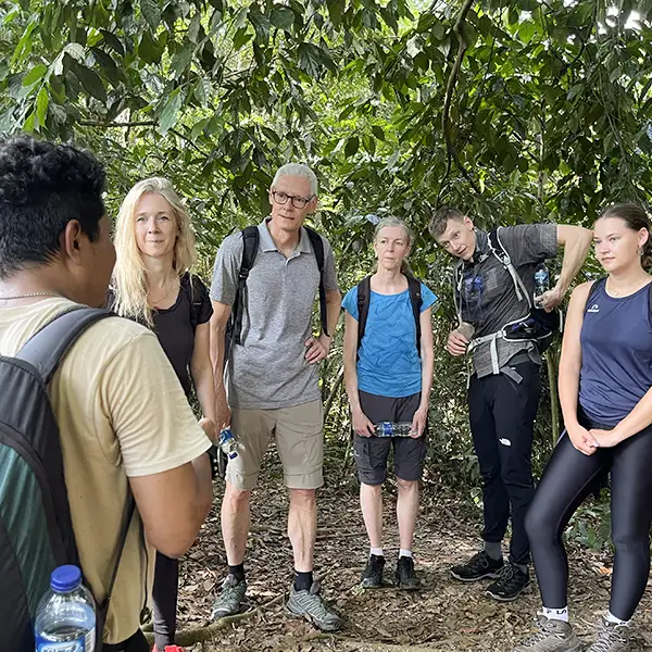 Group of hikers listening to a guide on a jungle trail surrounded by greenery.