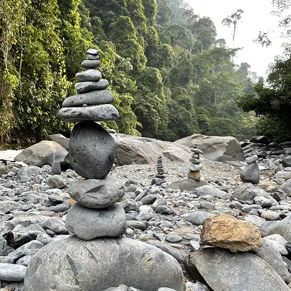 Stacks of smooth stones balanced carefully by a river in the Sumatran jungle, a symbol of harmony and balance in nature.