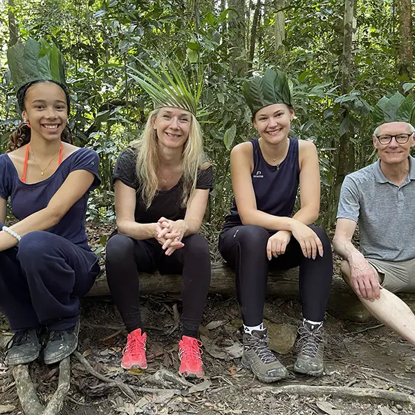 Trekkers resting on a fallen tree in the jungle, wearing natural leaf hats, with relaxed smiles after a hike