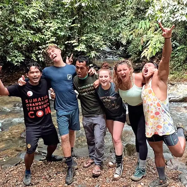 a group of energetic trekkers with arms around each other, making playful gestures by a rocky stream in the jungle, displaying a sense of camaraderie and adventure.