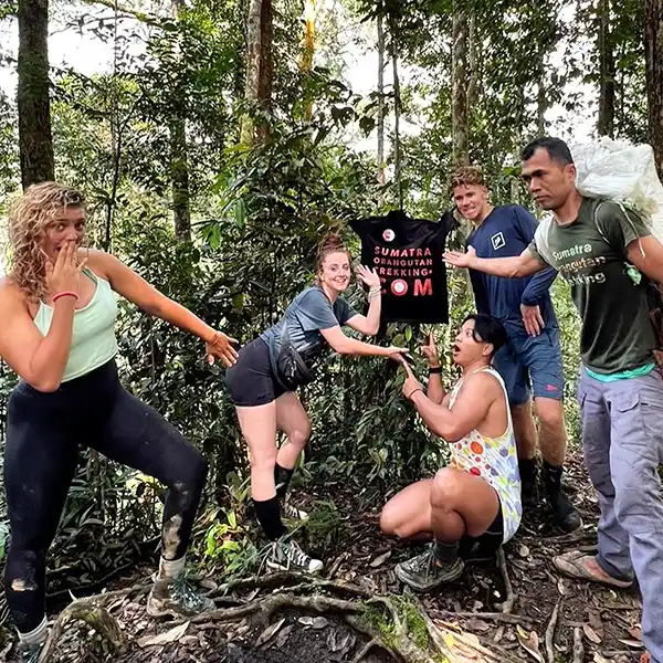 Tourists and a guide staging a playful scene in the jungle with surprised expressions and a 'Sumatra Orangutan Trekking' T-shirt as the focal point.