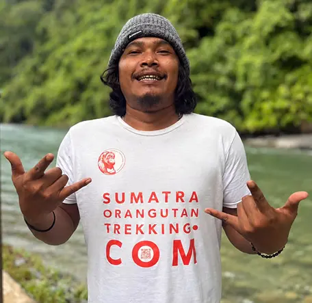 Brema smiling in a knitted hat and holding both hands out beside the river.