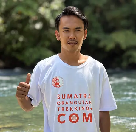 Isaq giving a thumbs-up beside the river in a Sumatra Orangutan Trekking T-shirt.