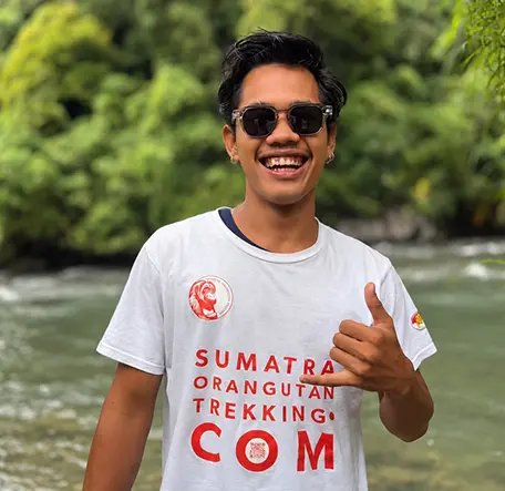Karan wearing sunglasses and smiling with one hand raised beside the river.