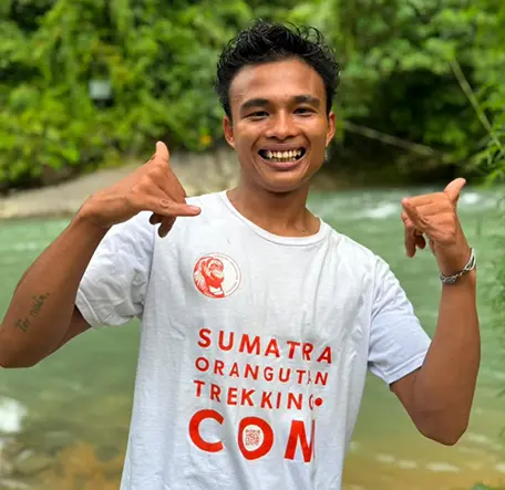 Ninta smiling and making playful gestures with both hands beside the river.