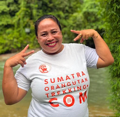 Jungle Mama, Anna, smiling and making peace signs with both hands beside the river.