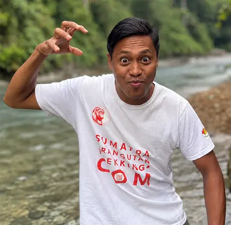 Nasir making a playful face and holding one hand like a claw beside the river.