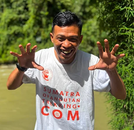 Sam smiling with both hands raised in a playful pose beside the river.