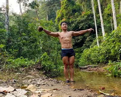 Eco workout trekking trainer Dedek is standing in the river in the jungle traning with a rock in his hand