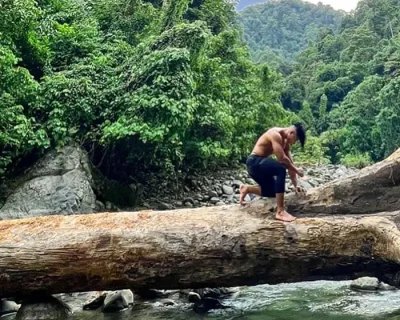 Indonesian Eco Workout Trekking trainer kneeling down at a big log that is hanging over the river