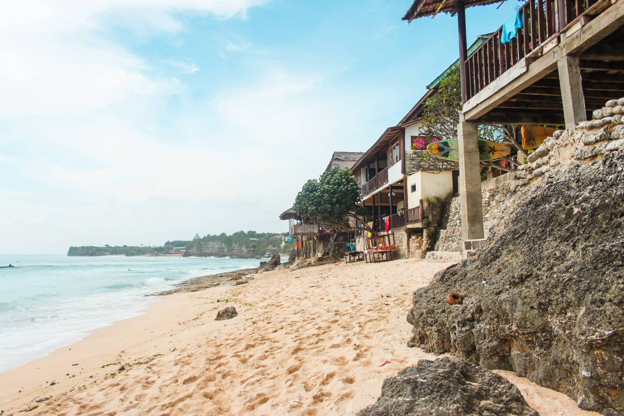 Where to stay in Bali: View of light sand and local warungs at an empty Bingin Beach, one of the best beaches in Uluwatu.