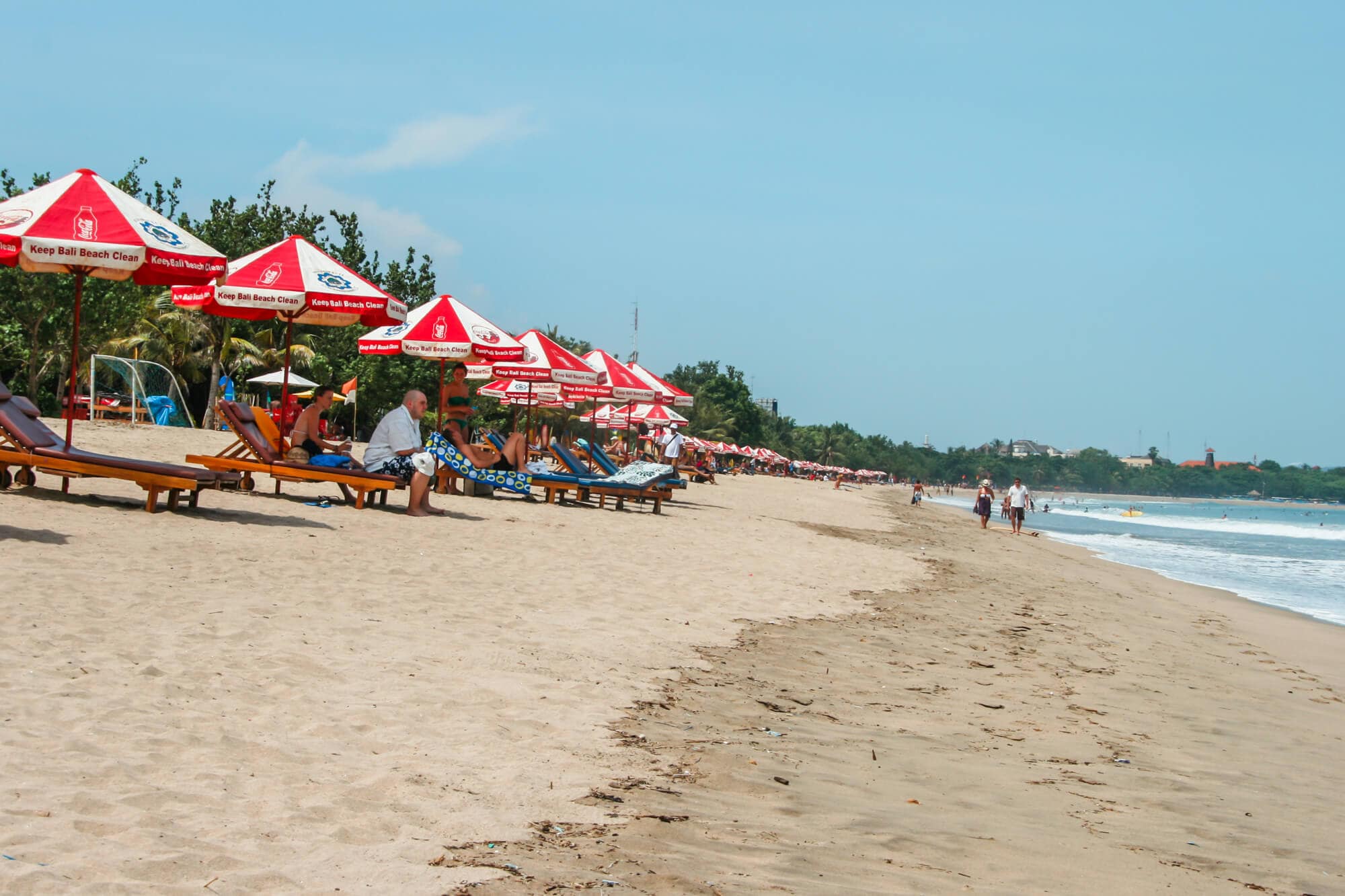 A row of sunbeds with red and white umbrellas on Kuta Beach, one of the best areas to stay in Bali for backpackers.