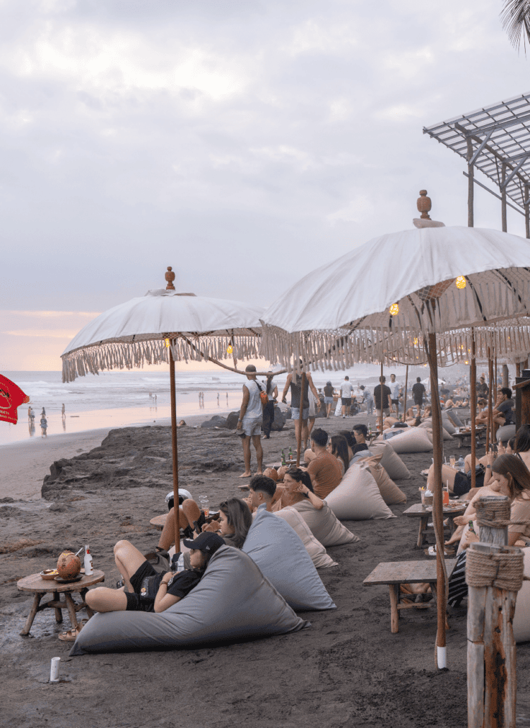 People sitting on bean bags under white umbrellas at bohemian La Brisa Beach Club on Echo Beach in Canggu right before sunset.