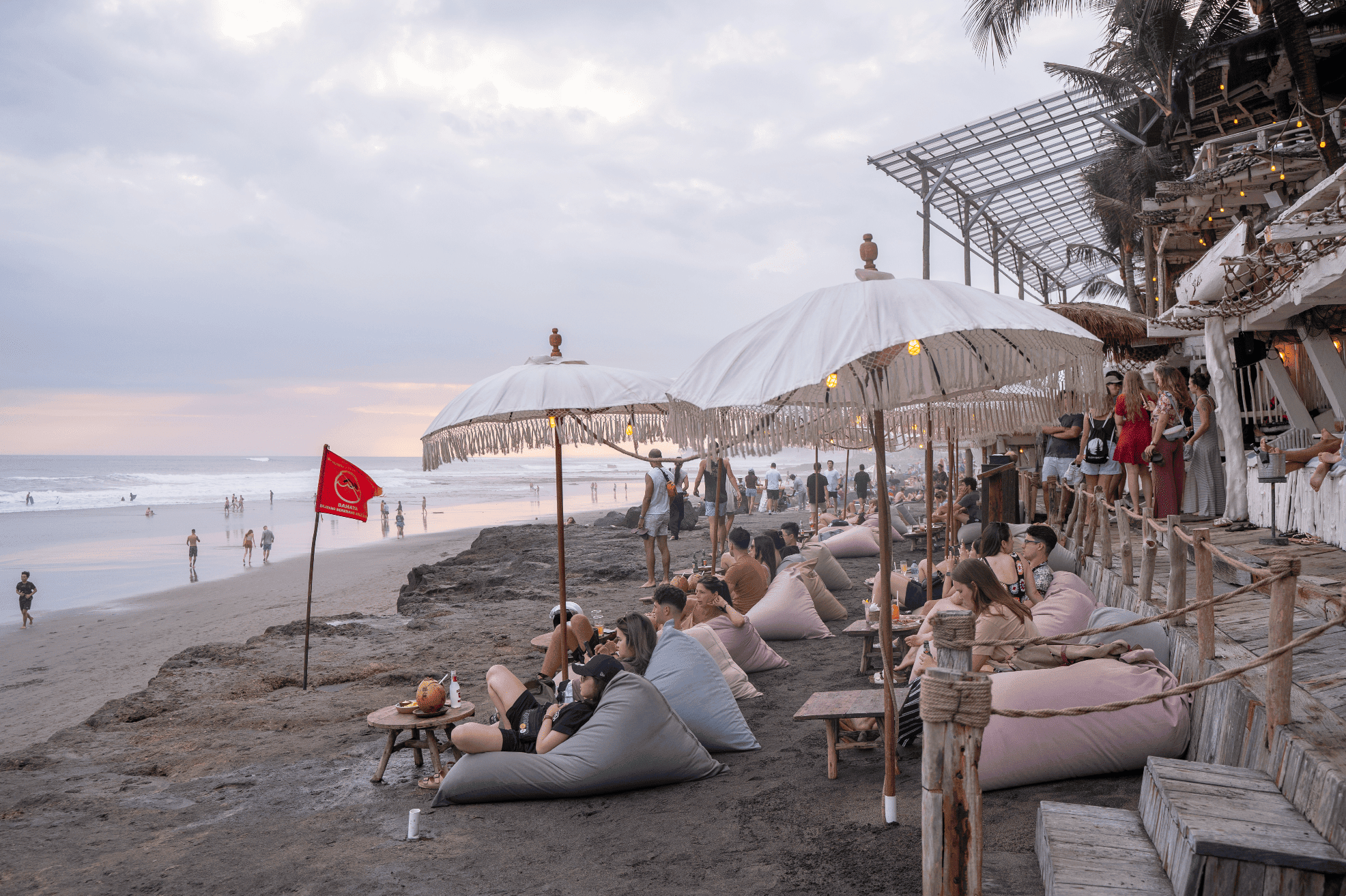 People sitting on bean bags under white umbrellas at bohemian La Brisa Beach Club on Echo Beach in Canggu right before sunset.