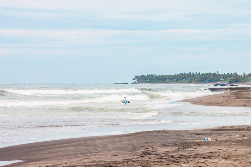 Surfer with colorful surfboard standing in the water looking at the waves at Echo Beach in Canggu.