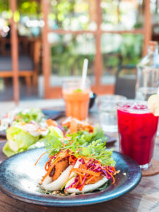 Bao buns with lettuce, carrots and red cabbage on a blue/grey plate with a red juice and a orange juice in the background at Knalpot, one of the best restaurants in Kuta Lombok.