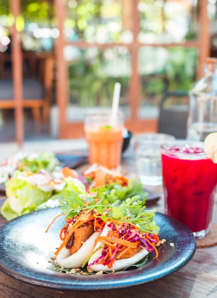 Bao buns with lettuce, carrots and red cabbage on a blue/grey plate with a red juice and a orange juice in the background at Knalpot, one of the best restaurants in Kuta Lombok.