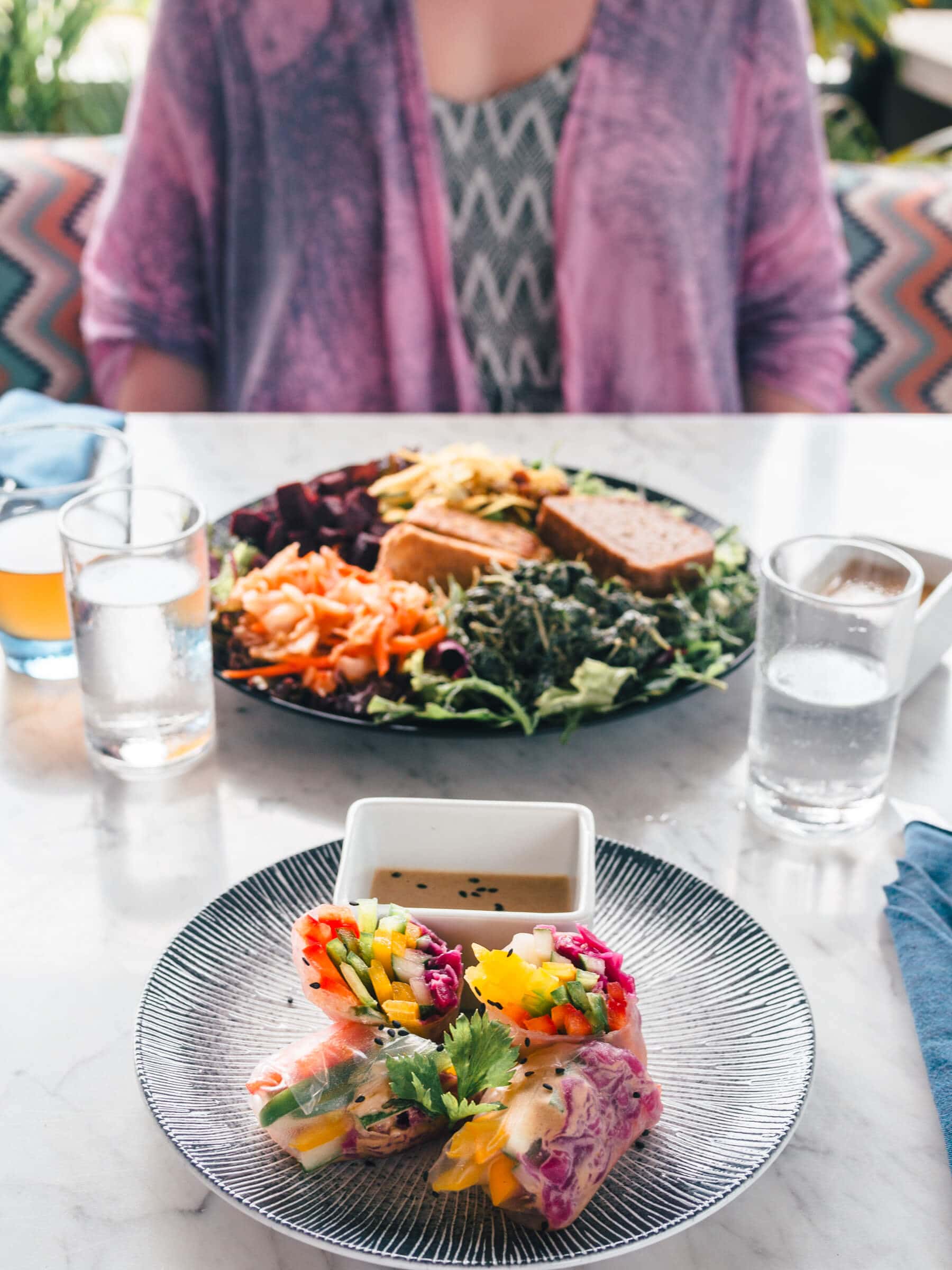 Colorful fresh spring rolls and a vegan vegetable salad, with a girl wearing a purple kimono in the background, at Terra a healthy vegan restaurant in Kuta Lombok.