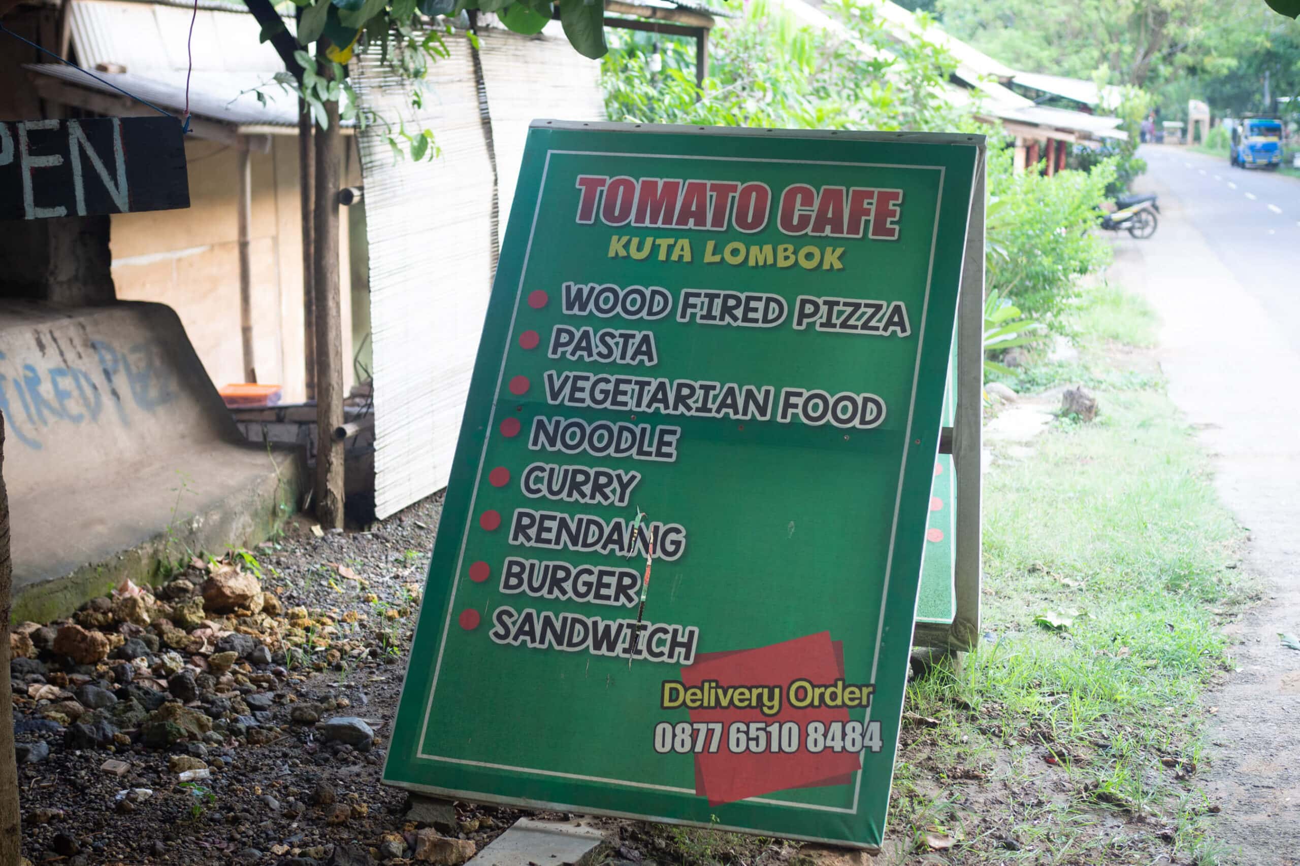 A green sign outside Tomato Cafe, one of the best restaurants in Kuta Lombok.