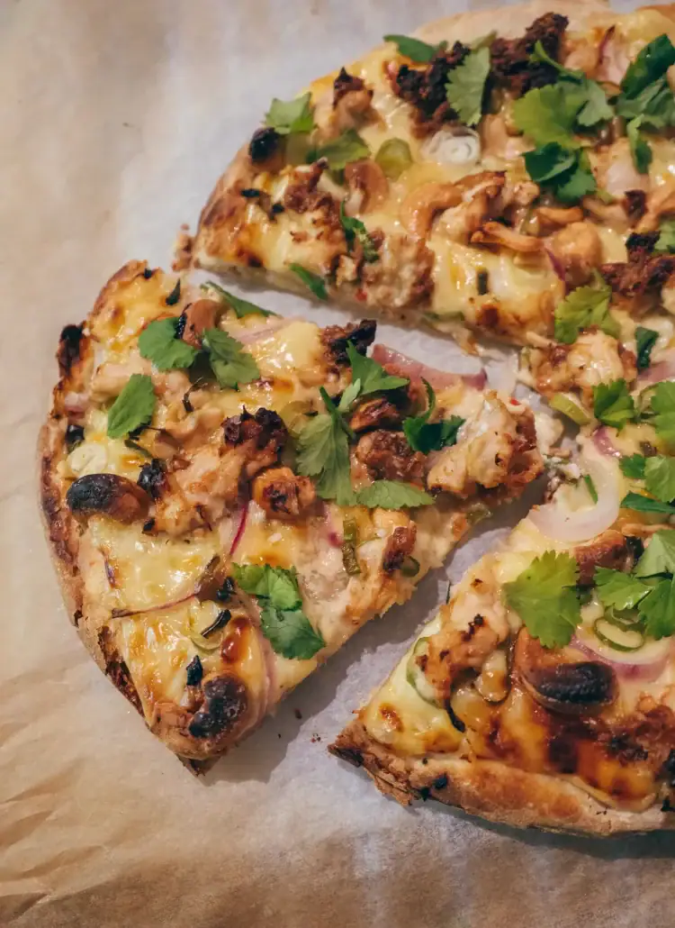 Close up of a slice cut out of a round Thai pizza with chicken, cashew nuts and coriander. Unique pizza recipe.