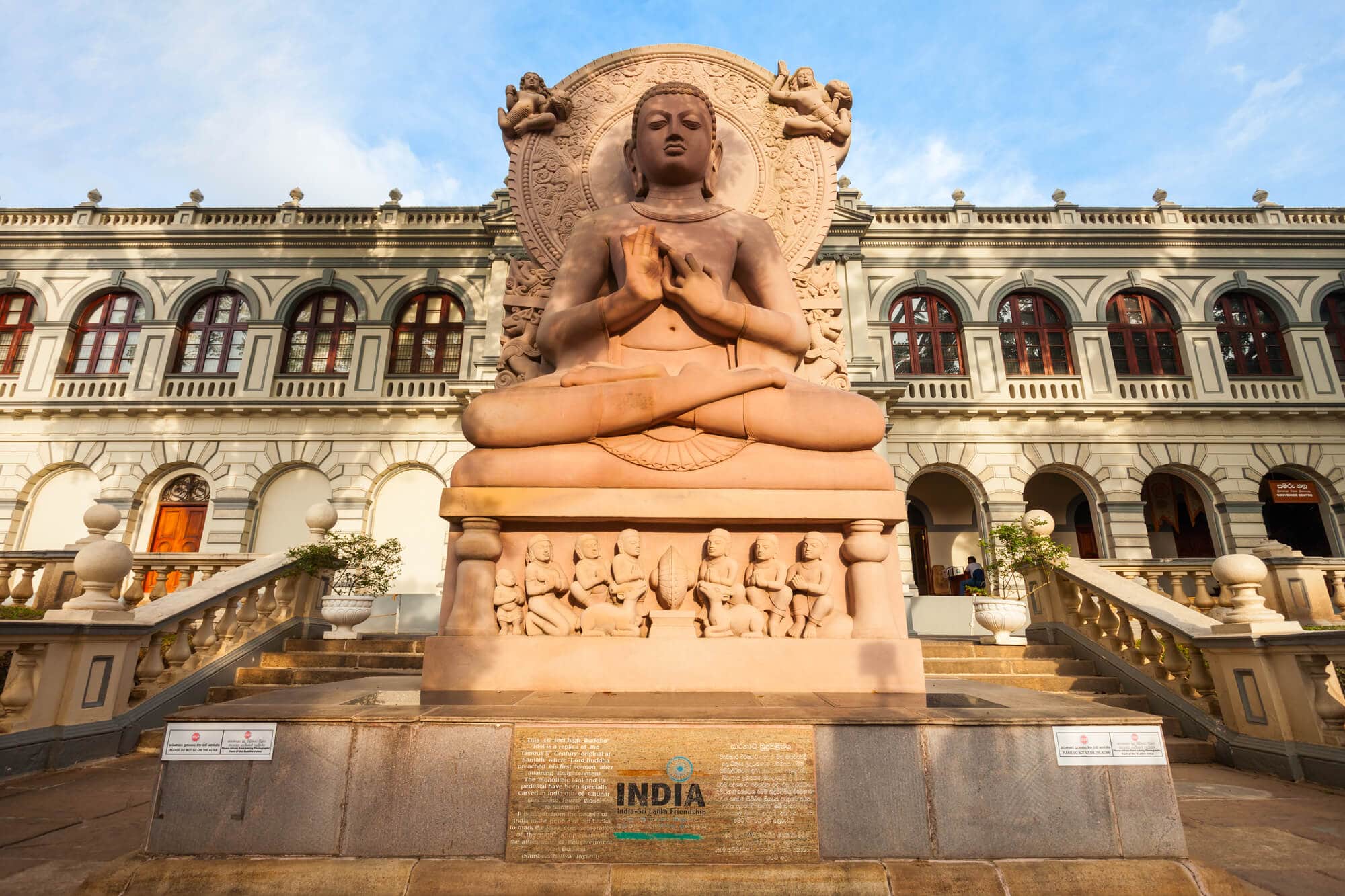 Large, light brown Buddha Statue in front of the imposing World Buddhist Temple housed in a former royal palace, one of the best places to visit in Kandy.