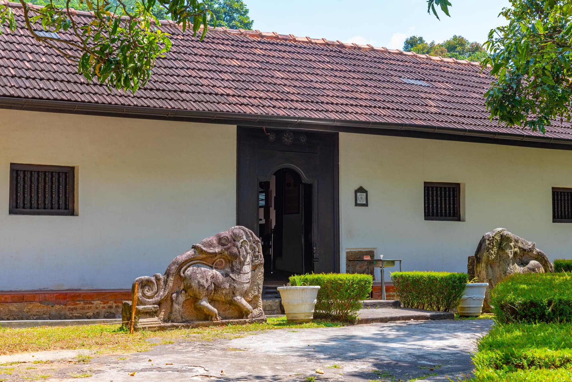 Thehe National Museum housed in a white building with a dark brown entrance area with two stone sculptures outside, one of the best places to visit in Kandy.