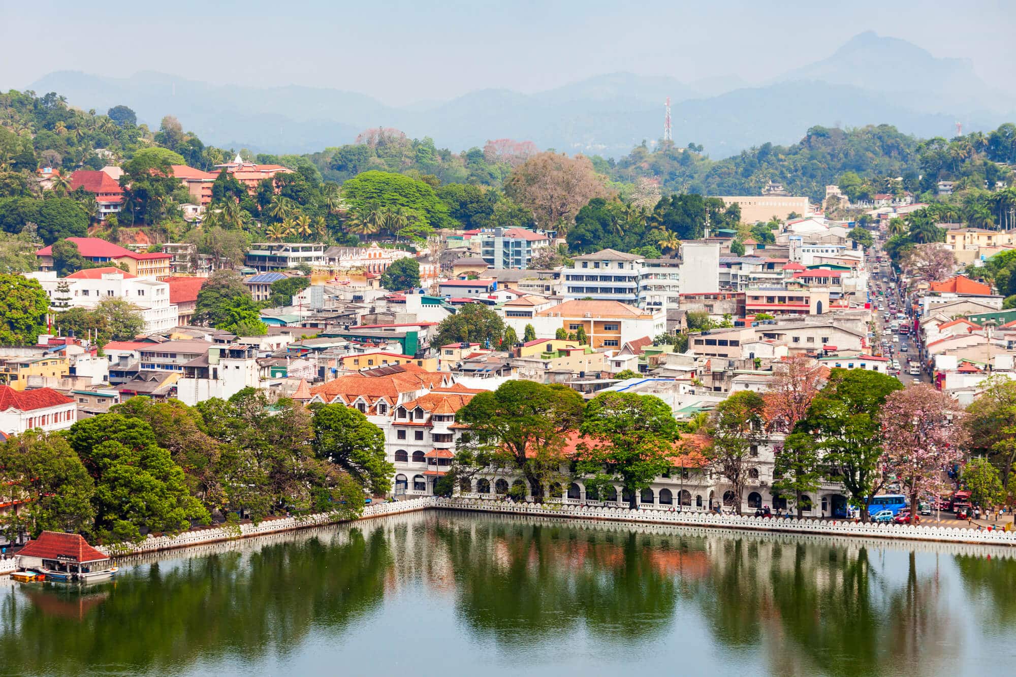 View of one corner of Kandy Lake lined by green trees with the city in the background, seen from Arthur's Seat, one of the best viewpoints in Kandy. 