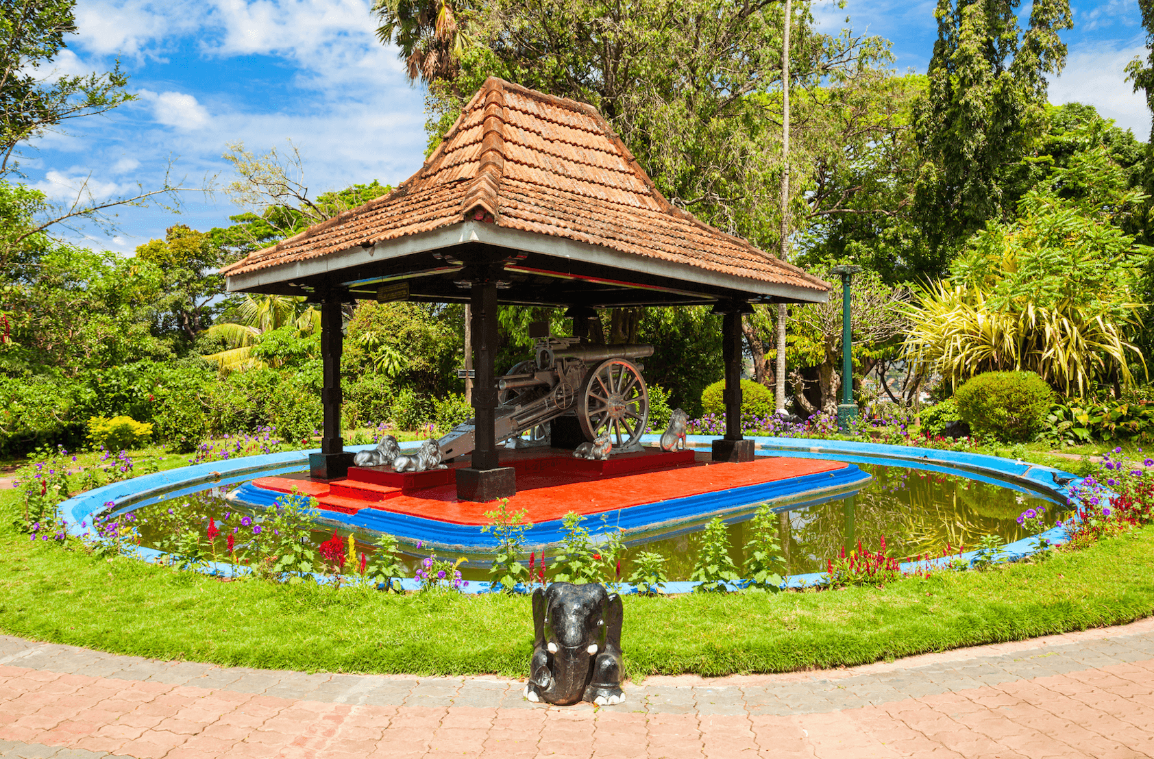 View of a gazebo in a small pond with a metal canon on a carriage under it in Wales Park (Royal Palace Park), one of the best places to visit in Kandy.