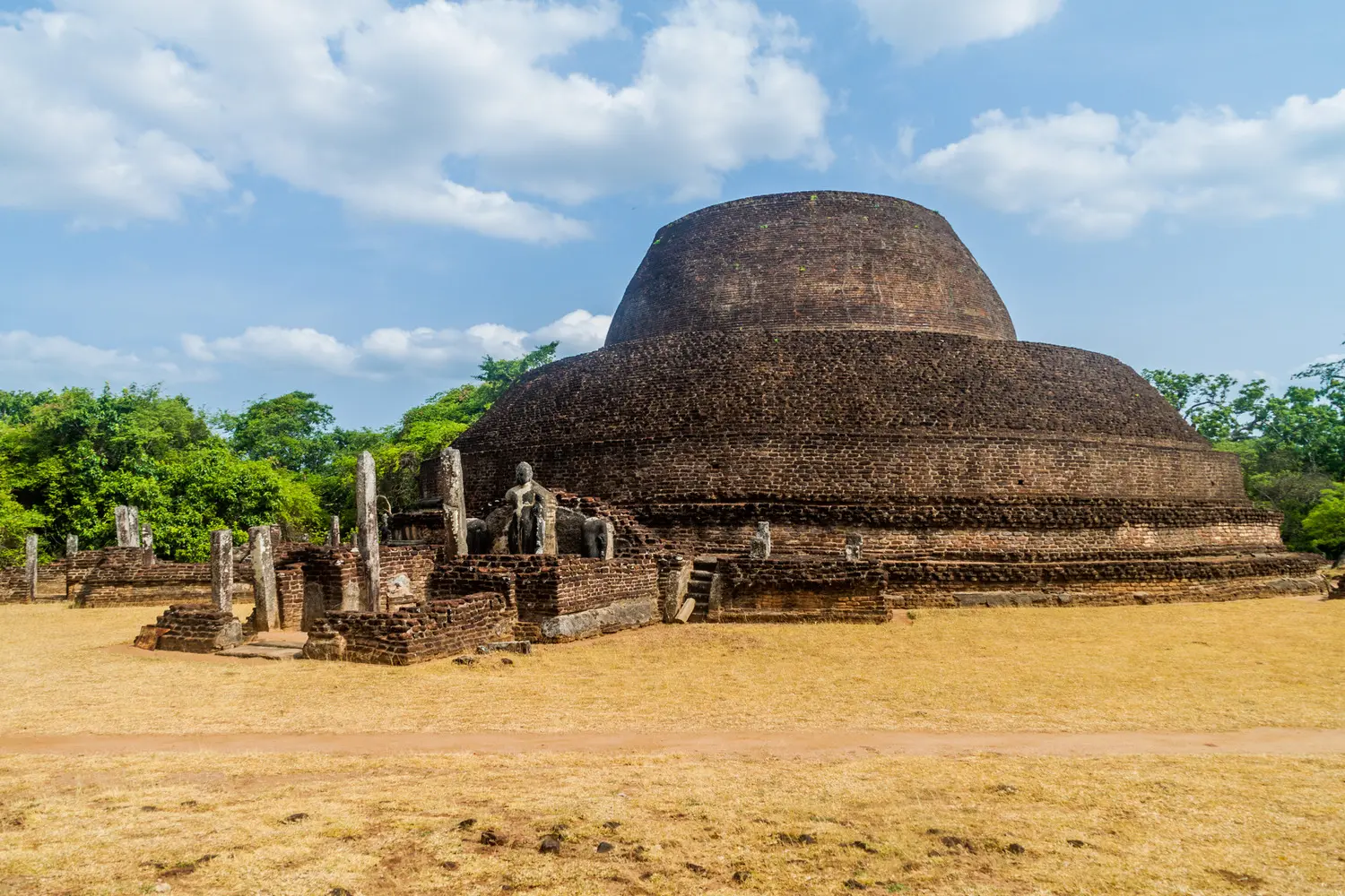 Large brick stupa ruin in two layers, with a Buddha statue and pillars at the entrance, in Polonnaruwa.