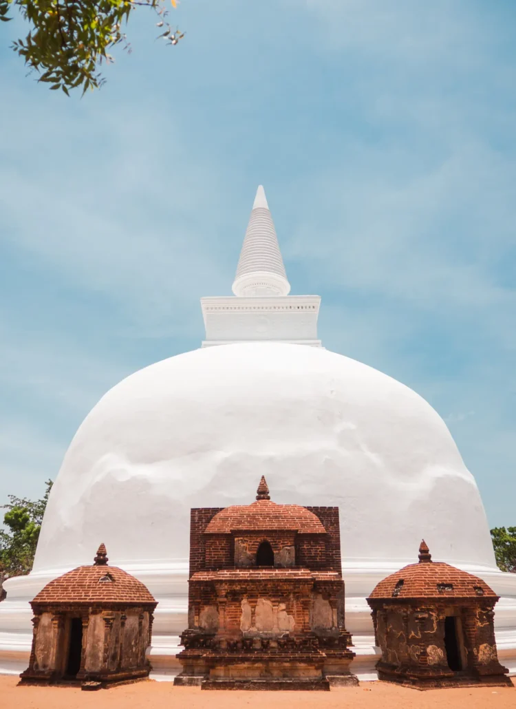 Bright white stupa Kiri Vehera with three brown brick shrines in front set against a blue sky in Polonnaruwa, Sri Lanka.