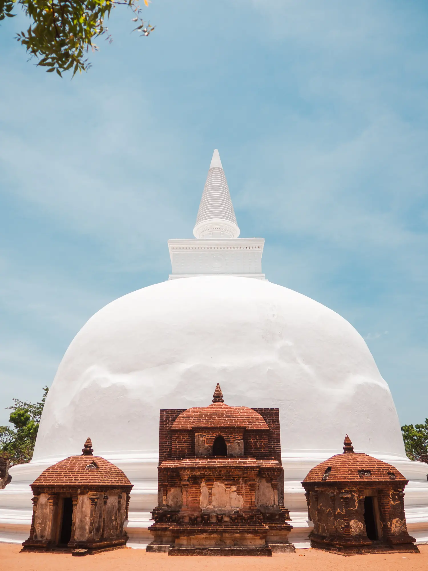 Bright white stupa Kiri Vehera with three brown brick shrines in front set against a blue sky in Polonnaruwa, Sri Lanka.